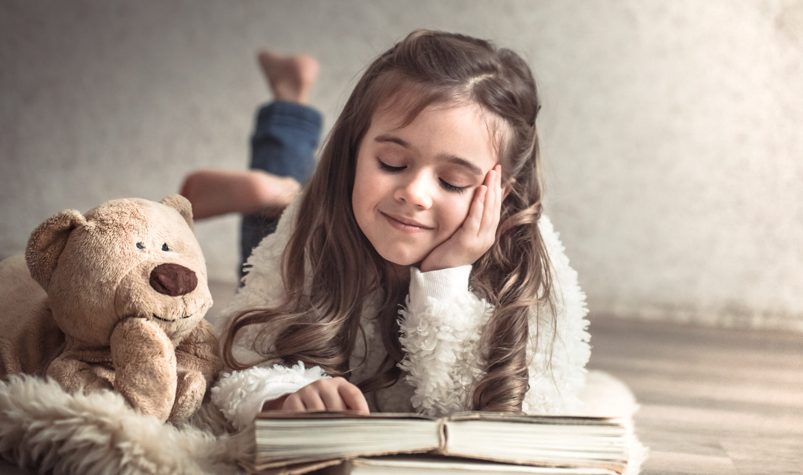 Ein kleines Mädchen liest mit ihrem Teddy in einem Buch – ein Bild für Freundschaft, Glück und Entspannung.